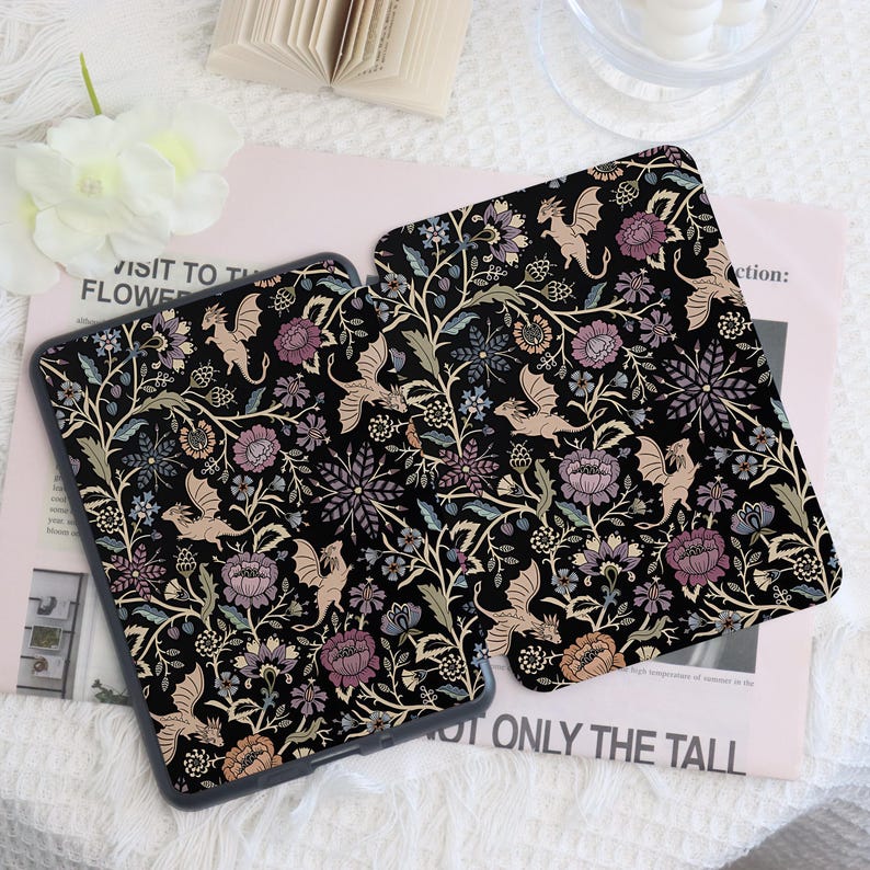 May include: Two black tablet cases with a floral and dragon pattern. The design features dragons, flowers, and foliage in shades of beige, purple, and green against a black background. The cases are on a light pink surface.