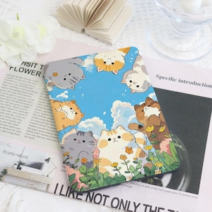 May include: A rectangular, blue-sky-themed phone case featuring cartoon cats. The case has a border of fluffy white clouds and a variety of adorable cats in different colors, including gray, orange, and white. The cats are surrounded by green grass and yellow flowers.