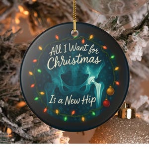 Pode incluir: Enfeite de Natal redondo com o texto "All I Want for Christmas Is a New Hip". O enfeite apresenta uma imagem de raio-x turquesa de uma articulação da anca, rodeada por uma grinalda de luzes e flocos de neve.