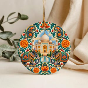 Peut inclure: Une décoration ronde en céramique illustrant le Taj Mahal entouré de deux éléphants. Le motif présente des fleurs orange vif, des motifs cachemire bleu sarcelle et un feuillage vert sur un fond crème, suspendu par un cordon doré.
