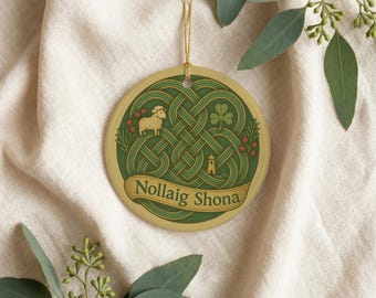 Könnte beinhalten: Ein runder Keramikschmuck mit einem grünen keltischen Knotenmuster, einem kleinen Schaf, einem Kleeblatt und einem Turm. Ein goldenes Band am unteren Rand zeigt den Text Nollaig Shona in dunkelgrüner Schrift. Der Schmuck hängt an einer goldenen Schnur.