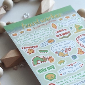 Puede incluir: Una hoja de pegatinas con fondo verde y varias ilustraciones y textos. Las pegatinas presentan una oruga, un tipo divertido, un escritorio de pie, un icono de tiempo de juego y otros diseños divertidos. El texto en las pegatinas incluye "handworker", "I showered", "ru my code?", "gaming time", "silly guy", "standing desk", "my beloved", "This pull request is still a work in progress", "public", "protected", "private", "sorry I am gamer", "approved", and "blocker".