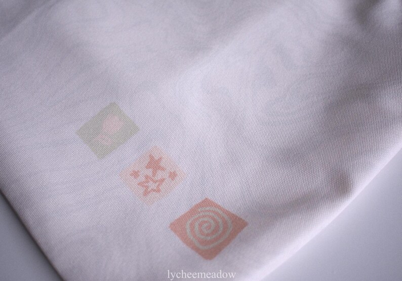 May include: White fabric tote bag with three pink and green floral designs. The designs are in the shape of squares and feature a swirl pattern.