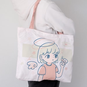 May include: A pink canvas tote bag featuring a cartoon illustration of a girl with blonde hair and a halo, holding a butterfly. The text "lychee meadow" is printed on the bottom of the bag.