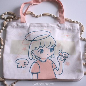 May include: A white tote bag with a pink handle and a cartoon illustration of a girl with a halo and wings. The girl is holding a butterfly and the text "lycheemeadow" is printed on the bottom of the bag.