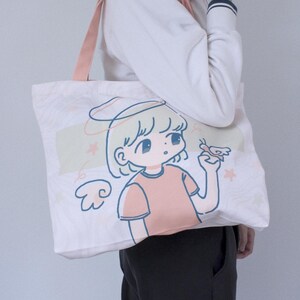 May include: A white canvas tote bag with a pink handle. The bag features a cartoon illustration of a girl with blonde hair and a halo, wearing a pink shirt and holding a butterfly. The text "lycheemeadow" is printed on the bottom of the bag.