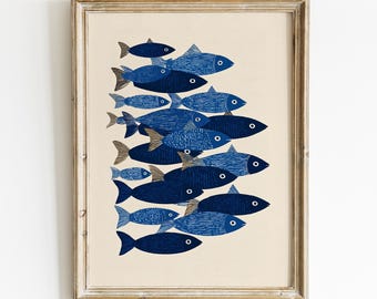以下が含まれることがあります： 青とネイビーの色合いの魚の群れが描かれた額入りのアートプリント。魚はクリーム色の背景に対して垂直に配置されています。アートワークは、明るい茶色の木製フレームに囲まれています。