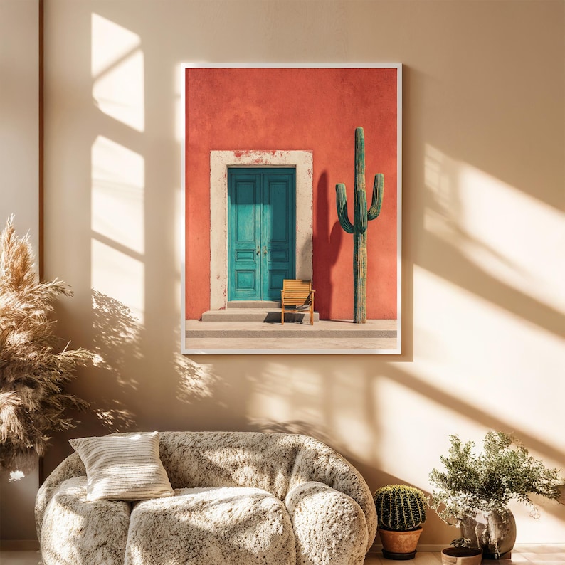 May include: A framed print featuring a vibrant scene of a teal door set in a red wall, with a cactus and a small wooden chair. The artwork evokes a Southwestern or desert aesthetic, with a bright, sunny ambiance.