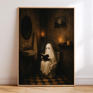 May include: A framed wall art print depicting a figure draped in a white sheet sitting on a toilet in a dimly lit bathroom. The figure holds an open book. The room features a sink, a mirror, a towel, candles, and a checkered floor pattern.