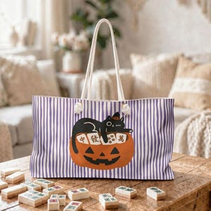 May include: A tote bag with white and purple vertical stripes featuring a graphic of a black cat lying on a jack-o'-lantern pumpkin with mahjong tiles. The pumpkin has a carved face and the tiles display the Chinese characters 中, 發, and 萬.