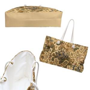 May include: A tote bag featuring a beige and brown pattern of lotus flowers and mahjong tiles with the letters TS in the corner. The bag has white rope handles, a solid beige base, and a plain white interior lining visible in the open view.