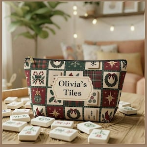 May include: A zipped pouch featuring a festive grid pattern of Christmas wreaths, candy canes, ornaments, and mahjong tiles. A central cream-coloured label displays the text Olivia's Tiles. The pouch is surrounded by scattered white mahjong tiles.