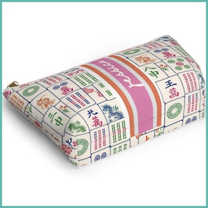 May include: A rectangular cosmetic bag with a zip. The bag has a cream background with a pattern of colourful Mahjong tiles. A pink stripe with the name "Jessica" is centred on the bag.