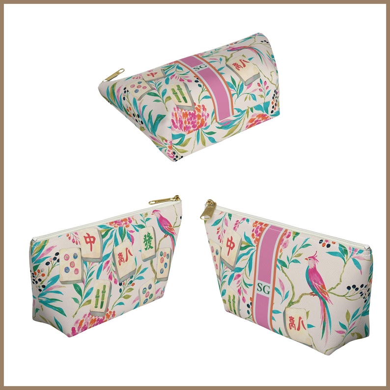 May include: Three zippered pouches featuring a cream background with a colorful pattern of mahjong tiles, pink birds, and green foliage. A vertical pink stripe on the pouches displays the letters SG in a white font, with gold-toned metal zippers.