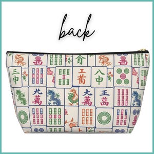 May include: A cream-coloured zippered pouch with a pattern of colourful Mahjong tiles. The tiles display various symbols, dragons, and Chinese characters. The word "back" is written in black script above the pouch.