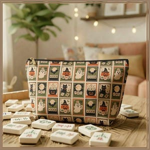 May include: A zippered pouch featuring a repeating pattern of rectangular postage stamp-style illustrations. The design includes Halloween-themed motifs such as ghosts, black cats, pumpkins wearing hats, and cauldrons, set against a cream background.