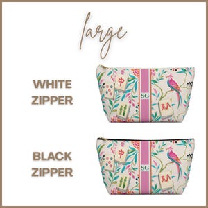 May include: Two large zippered pouches featuring a cream background with a colorful pattern of mahjong tiles, tropical birds, and foliage. A central vertical pink stripe displays the initials SG. One pouch has a white zipper, the other black.