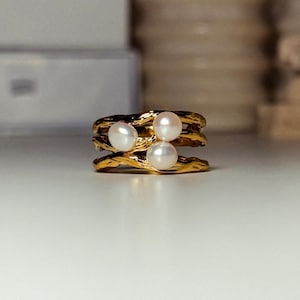 May include: A gold ring with three white pearls set in a twisted band design.