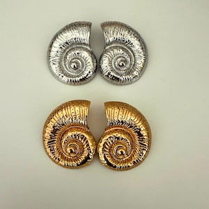 May include: A pair of gold and silver shell-shaped earrings. The earrings are large and have a textured surface.