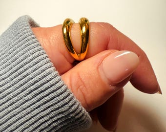 May include: A gold-toned ring with a unique intertwined design. The ring is worn on a finger.