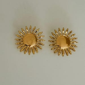 May include: A pair of gold sun-shaped earrings with a textured design.