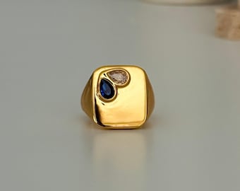 May include: A gold signet ring with a square face featuring a blue and white pear-shaped gemstone design.