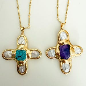 May include: Two gold necklaces with cross pendants. One pendant features a turquoise stone surrounded by white mother-of-pearl, while the other pendant features a purple amethyst stone surrounded by white mother-of-pearl.
