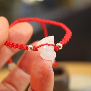 May include: A red string bracelet with a white jade pendant. The pendant is carved in the shape of a leaf.