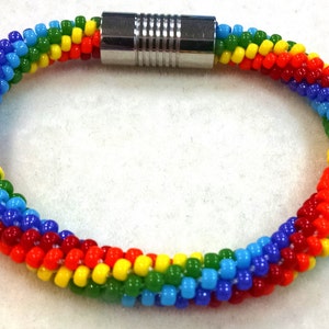 Pode incluir: Um bracelete de contas de arco-íris com um fecho magnético prateado. O bracelete é feito com pequenas contas coloridas em forma de espiral.