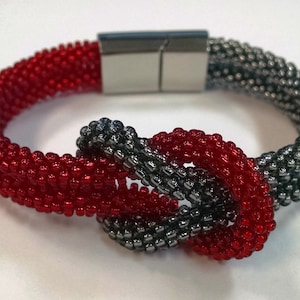 Peut inclure: Un bracelet en perles rouges et grises avec un nœud et un fermoir magnétique.