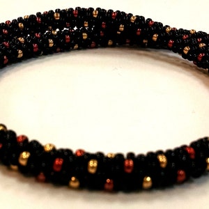 May include: A close-up of a black, gold, and red beaded necklace. The necklace is made of small, round beads that are woven together in a spiral pattern.
