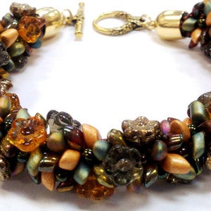 Puede incluir: Un brazalete de cuentas con un cierre dorado. El brazalete está hecho con una variedad de cuentas marrones, naranjas y verdes, incluyendo cuentas con forma de flor.