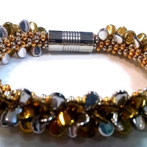May include: A gold and silver beaded bracelet with a magnetic clasp. The bracelet is made of small, round beads that are arranged in a pattern of alternating gold and silver.