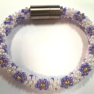 May include: A white and purple beaded bracelet with gold accents and a magnetic clasp.