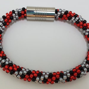 May include: A red, black, and silver beaded bracelet with a magnetic clasp.