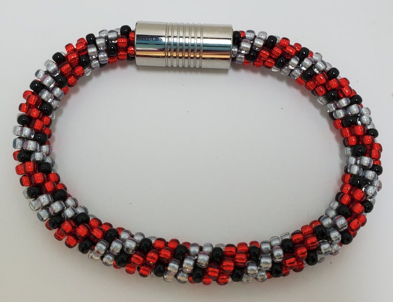 May include: A red, black, and silver beaded bracelet with a magnetic clasp.