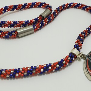 May include: A red, white, and blue beaded necklace with a silver magnetic clasp. The necklace has a silver charm with a red, white, and blue star design.