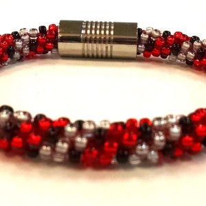 May include: A red, black, and silver beaded bracelet with a magnetic clasp.