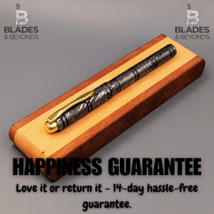 Puede incluir: Un bol&iacute;grafo estampado con detalles dorados descansa sobre un portal&aacute;pices de madera. El bol&iacute;grafo presenta un dise&ntilde;o detallado en tonos grises y negros. El portal&aacute;pices est&aacute; hecho de madera clara y oscura. El texto "HAPPINESS GUARANTEE" es visible.