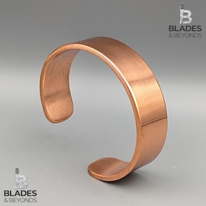 May include: A copper-coloured cuff bracelet with a brushed metal finish. The open-ended design features a smooth, curved shape. The bracelet is a simple, yet elegant piece of jewellery.