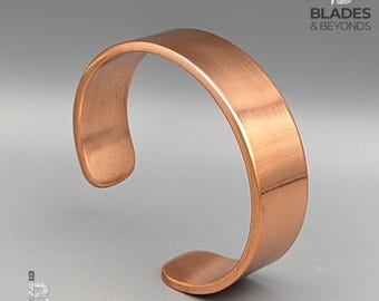 以下が含まれることがあります： 銅色のカフブレスレット。つや消し金属仕上げ。オープンエンドのデザインは、滑らかで湾曲した形状が特徴です。シンプルでありながらエレガントなジュエリーです。