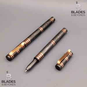 以下が含まれることがあります： 濃い木目模様と銅色のアクセントが付いた3本のペン。1本のペンは開いており、筆記チップが見えます。ペンのキャップとクリップも銅色です。「Blades & Beyonds」のロゴが右上と左下にあります。