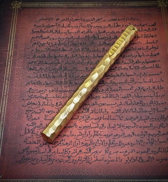 A ballpoint pen hand-forged from layered Damascus steel with 12K gold coating — the kind of desk object that stops visitors mid-sentence.