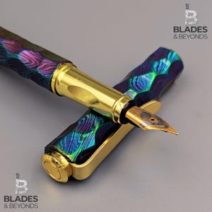 Op de afbeelding: Een luxe vulpen met een goudkleurige penpunt en accenten. De pen heeft een patroon van iriserende kleuren, waaronder blauw, groen en paars. De pen is gedeeltelijk gedemonteerd, met de dop ernaast.