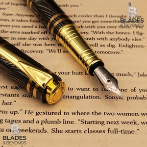 May include: Close-up of a black and gold fountain pen with intricate detailing. The pen features a patterned barrel and gold accents. The nib is visible, resting on a page of printed text. The pen is a writing instrument.
