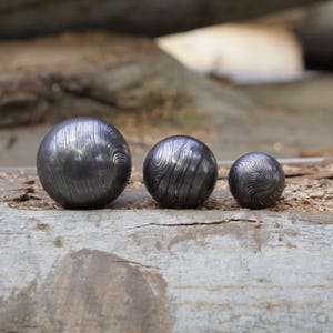 May include: Three round metal spheres with a swirling pattern, arranged in order of size from largest to smallest on a wooden surface.