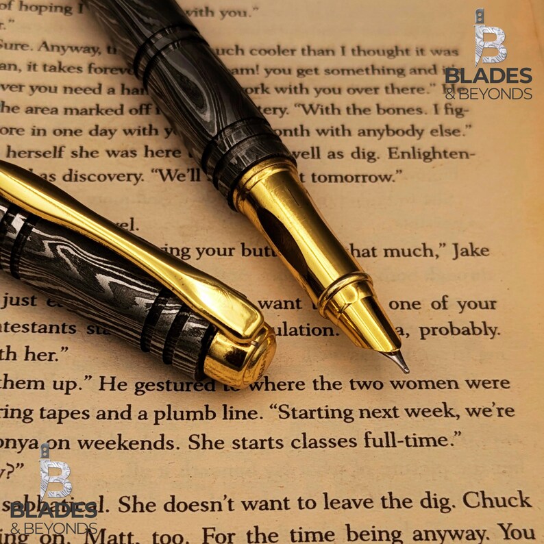 Puede incluir: Primer plano de dos plumas estilogr&aacute;ficas de lujo. Las plumas tienen un cuerpo con un patr&oacute;n negro y plateado con detalles dorados. Las puntas son visibles y las plumas descansan sobre una p&aacute;gina de texto impreso.