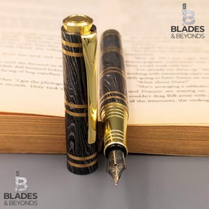 May include: A luxury fountain pen with a black and gold design. The pen features a patterned barrel with gold accents and a gold-colored nib. The pen's cap is off, revealing the nib and the pen's intricate design. The pen is set against a blurred background.