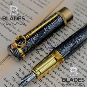 May include: A luxury fountain pen with a black and silver patterned barrel, gold accents, and a decorative clip. The pen is displayed on a book, showcasing the "Blades & Beyonds" logo.