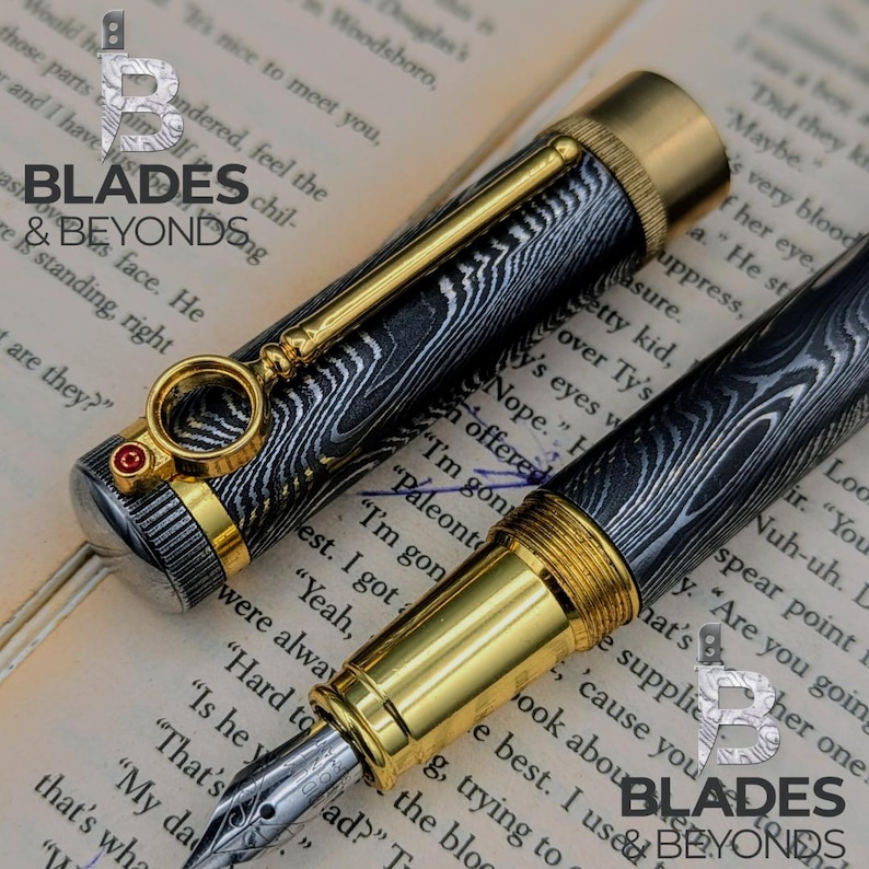 May include: A luxury fountain pen with a black and silver patterned barrel, gold accents, and a decorative clip. The pen is displayed on a book, showcasing the "Blades & Beyonds" logo.